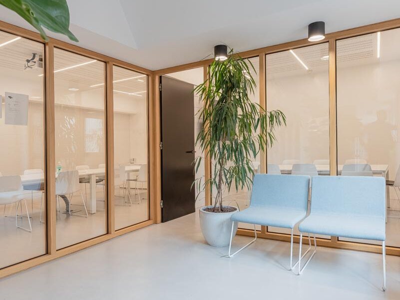 Sala de espera con sillas grises y planta. Al fondo, dos salas de reuniones.